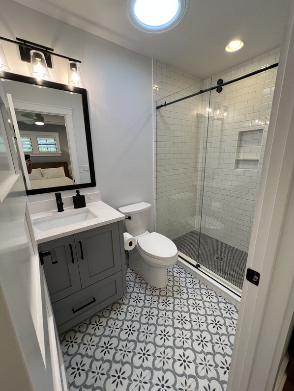 Et moderne badeværelse med hvid vask, underskab, toilet og brusekabine med glasvægge.