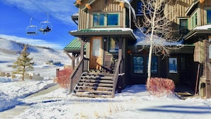 Un chalet en bois avec un escalier menant à l’entrée, entouré de neige.