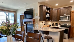 Une cuisine moderne avec des meubles de couleur sombre en bois, un îlot central doté de tabourets, un four à micro-ondes encastré et une cheminée en pierre.