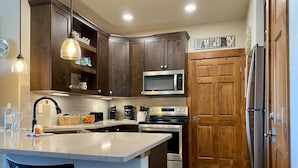 Une cuisine moderne avec des meubles de rangement en bois foncé, un four à micro-ondes en acier inoxydable, un four encastré et une porte en bois.