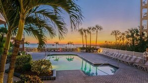 A pool area with a sunset view, palm trees, and lounge chairs.