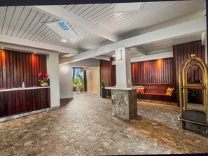 Un hall d’entrée avec un sol en pierre, des murs lambrissés en bois, un comptoir d’accueil et un banc.