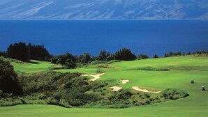 Ein Golfplatz mit Blick auf das Meer und die Berge im Hintergrund.