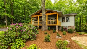 A cabin with a wooden porch, stone foundation, and a small attached building. -  Peaceful and luxurious living with spectacular views  (Spruce Pine)