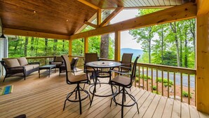 A covered outdoor area with wooden flooring, a round table, and several chairs. -  Peaceful and luxurious living with spectacular views  (Spruce Pine)