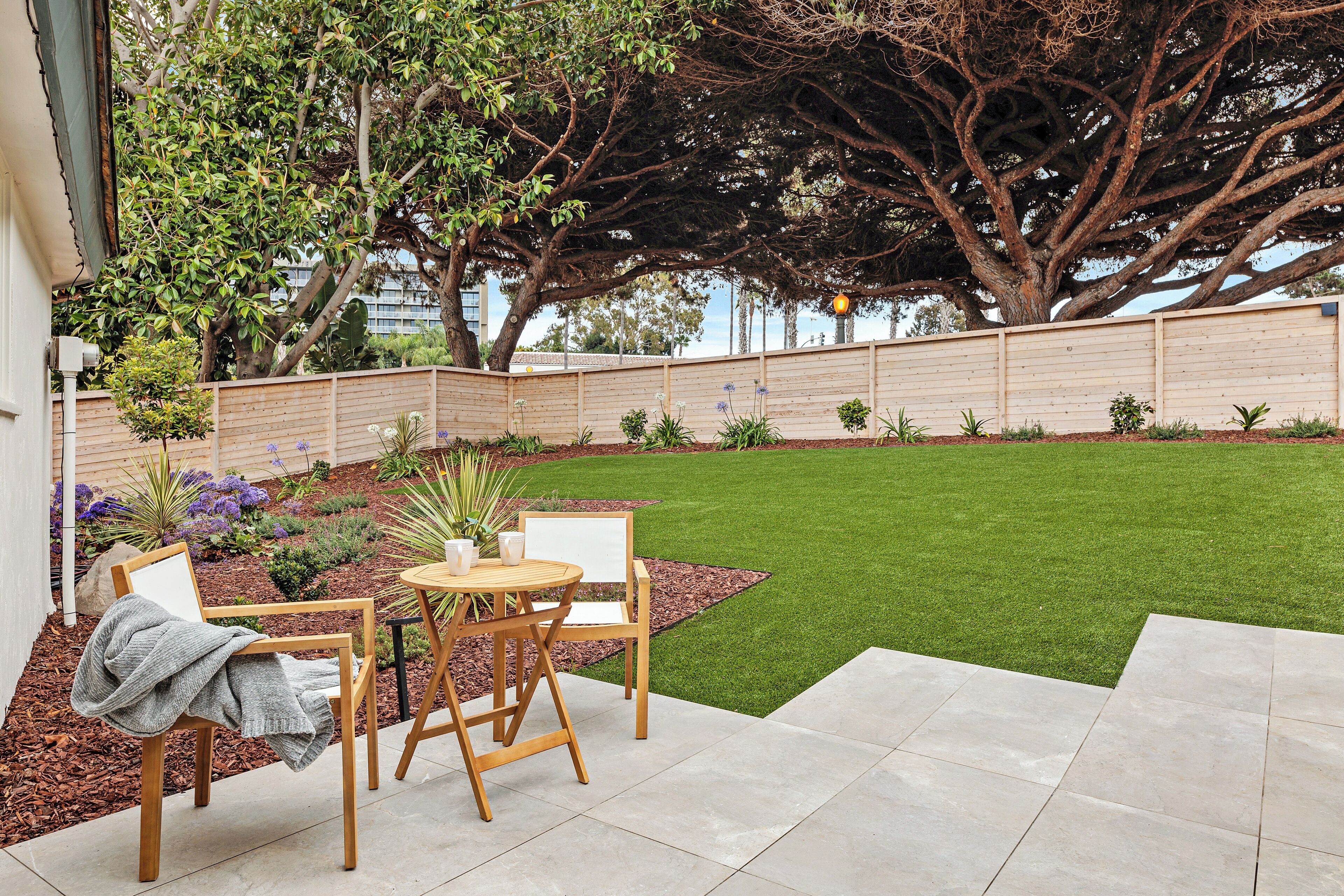 A patio with a table and chairs, a neatly trimmed lawn, and a wooden fence.