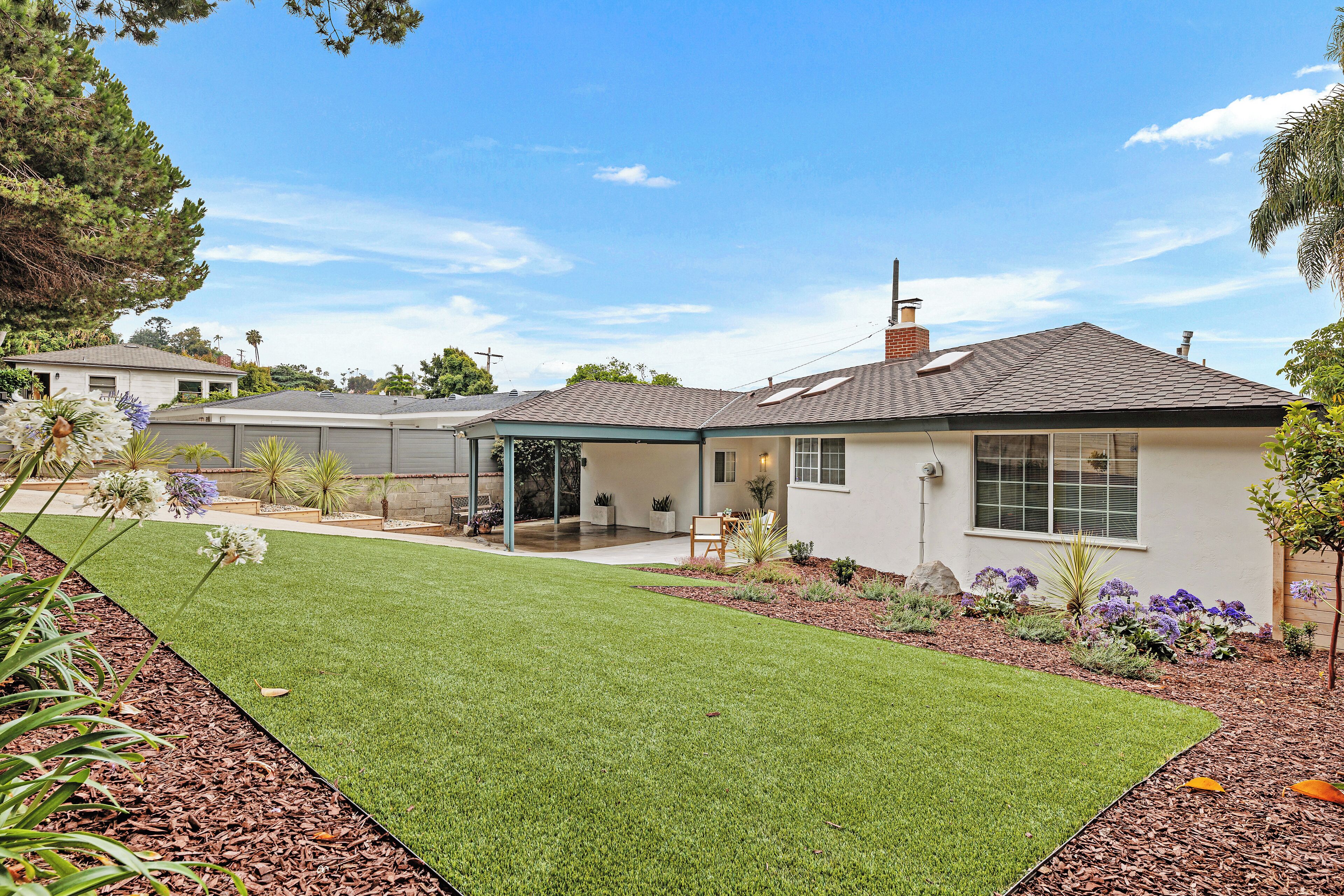 A single-story house with a covered patio, a well-maintained lawn, and a variety of plants and flowers.