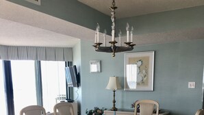 Un comedor con una mesa de vidrio rodeada por seis sillas, una araña y un cuadro en la pared.