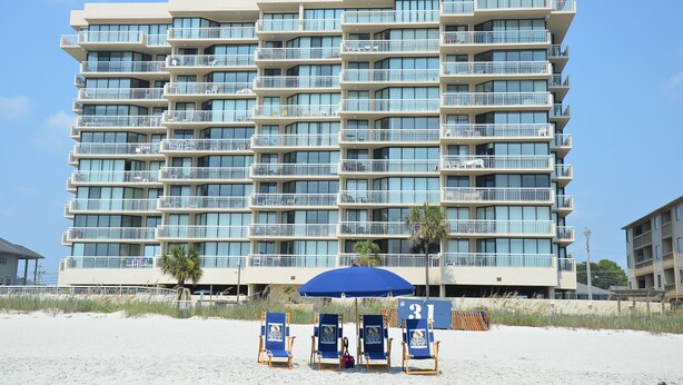 Un hotel de varios pisos con balcones, una sombrilla y sillas de playa.