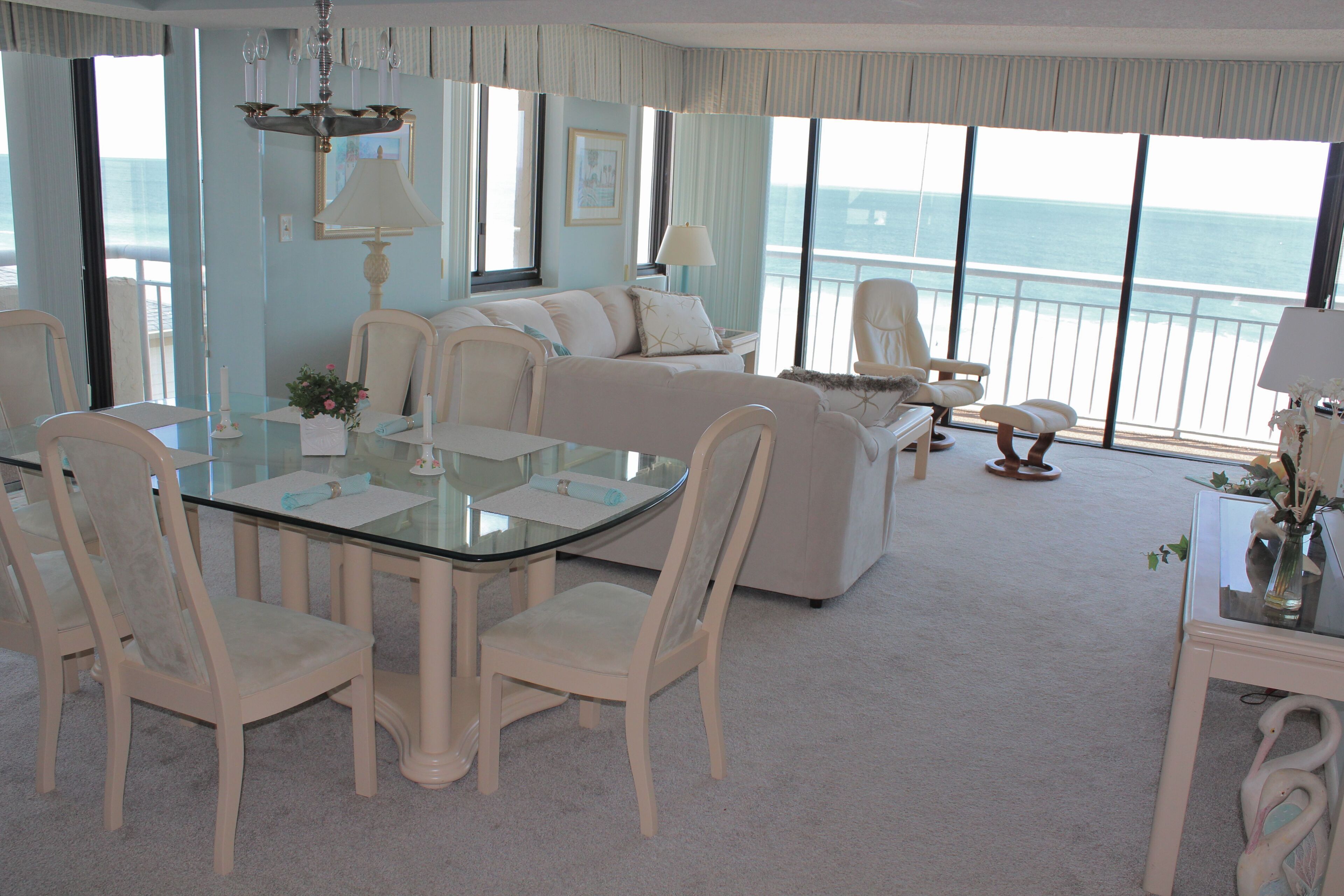 A spacious room with a dining table, chairs, a sofa, and a view of the ocean.