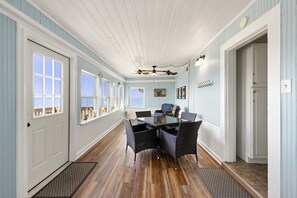A hallway with a dining area featuring wicker chairs and a table, wooden floors, and a ceiling fan.