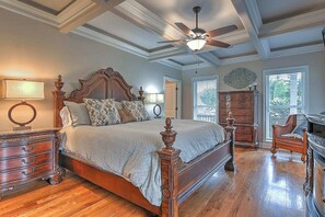 Ein Schlafzimmer mit einem großen Bett, Holzmöbeln, einem Deckenventilator und Blick durch ein Fenster.