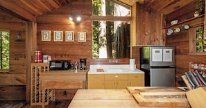 L’intérieur d’un chalet en bois comprend un coin cuisine équipé d’un réfrigérateur, d’un four à micro-ondes, d’une machine à café et d’une table en bois.