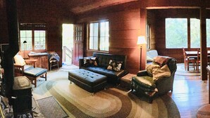 A cozy cabin interior with a fireplace, a sofa, a dining table, and a kitchen area with a sink and jars. - The Treehouse - a Romantic Russian River Retreat (Guerneville)