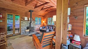 L’intérieur chaleureux d’un chalet avec une cheminée en pierre, des meubles en bois et une vue sur l’extérieur grâce à de grandes fenêtres.