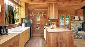Une cuisine rustique, située dans une cabane en bois, avec un îlot central, un réfrigérateur, une cuisinière et une cheminée en pierre.