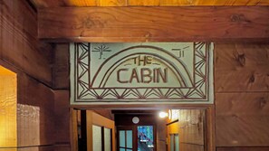 A wooden cabin interior with a sign reading 'THE CABIN' above a doorway.