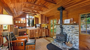 A wooden cabin interior with a stone fireplace, wooden bar, and seating area.