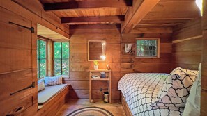Ein Schlafzimmer in einer Holzhütte mit Bett, Bank, Nachttisch, Lampe und Fenstern.