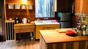 A wooden cabin kitchen with a large window, wooden cabinets, a sink, and a refrigerator. - The Treehouse - a Romantic Russian River Retreat (Guerneville)