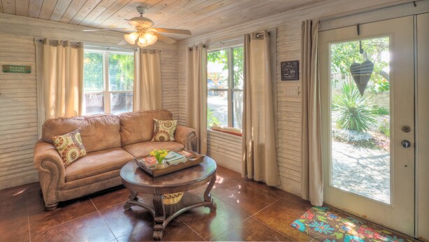 A cozy room with a wooden ceiling, a brown leather sofa with patterned cushions, a small round table with a tray, and a door leading outside. - 2 Blocks From Marketplatz & The Heart Of Main Street Shopping And Dining! (Fredericksburg)