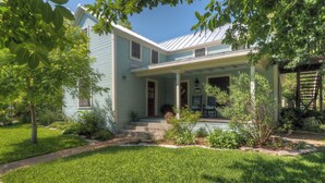A two-story house with a covered porch, a small garden, and a clear blue sky. - 2 Blocks From Marketplatz & The Heart Of Main Street Shopping And Dining! (Fredericksburg)