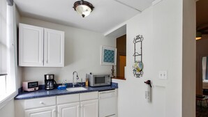 A compact kitchen with white cabinets, a blue countertop, a microwave, a coffee maker, and a sink. - Colonial Park Retreat! Historic District Prime Location! (Savannah)