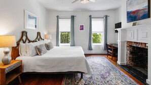 A bedroom with a bed, a nightstand, a lamp, a fireplace, and a ceiling fan. - Colonial Park Retreat! Historic District Prime Location! (Savannah)