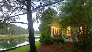 Una cabaña junto al lago con un porche, rodeada de árboles y un estanque.