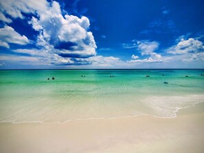 Ein Strand mit klarem türkisblauem Wasser, einem Sandufer und ein paar Personen im Wasser.