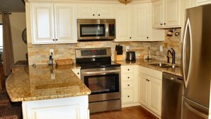 A kitchen with white cabinets, granite countertops, stainless steel appliances, and a stone backsplash. - Oceanfront Pet Friendly 3 BR Condo (North Myrtle Beach)