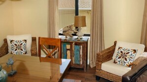 A cozy living room with a wooden table, two wicker chairs, a small side table with a lamp, and patterned cushions. - Oceanfront Pet Friendly 3 BR Condo (North Myrtle Beach)