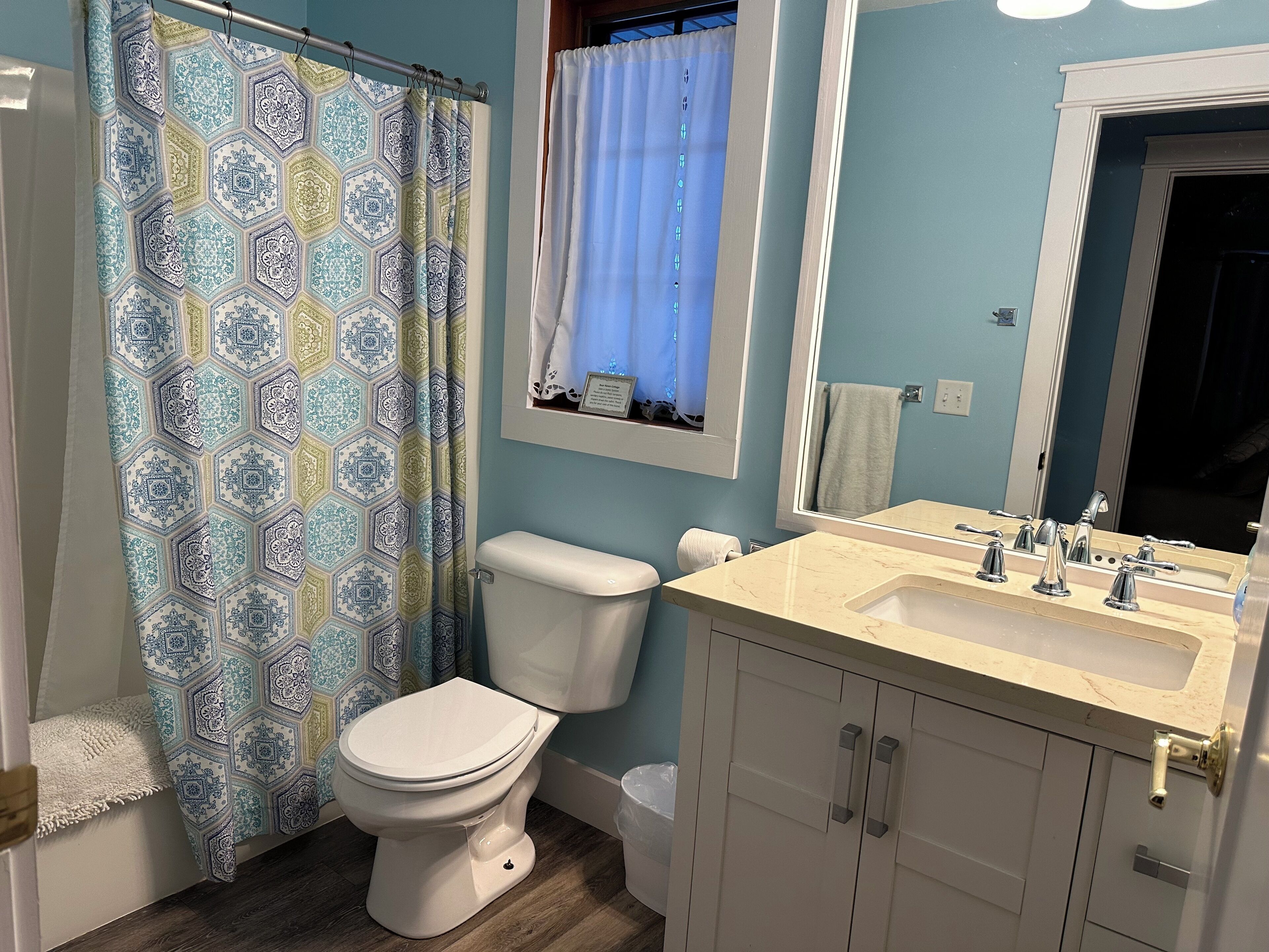 Une salle de bain équipée de toilettes, d’un lavabo, d’un miroir et d’un rideau de douche à motifs.