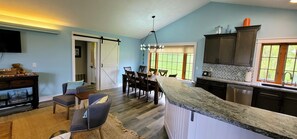 A kitchen with a large island, dark cabinets, and a view of the outdoors. - Bear Haven Cottage at Glen Lake Narrows (Glen Arbor)