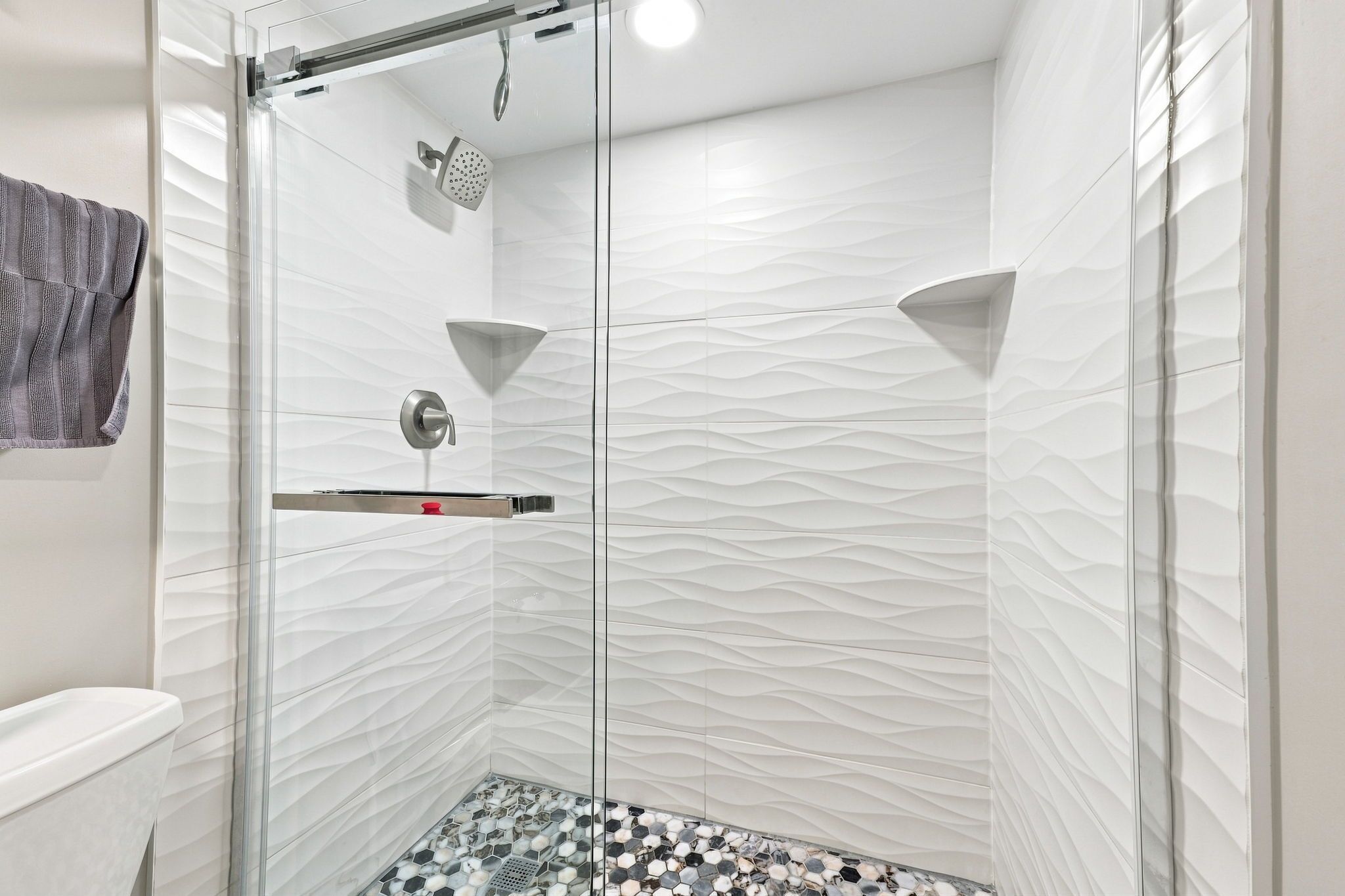 Una ducha moderna con puerta de cristal, cabezal de ducha manual y cabezal de ducha tipo lluvia.