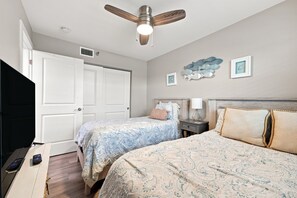 Een slaapkamer met twee bedden, een plafondventilator, een televisie en een dressoir.