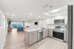 A modern kitchen with a central island, stainless steel appliances, and a view to the sea.