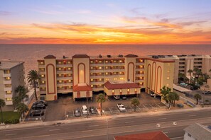 A multi-story hotel with a parking lot and a view of the ocean at sunset.