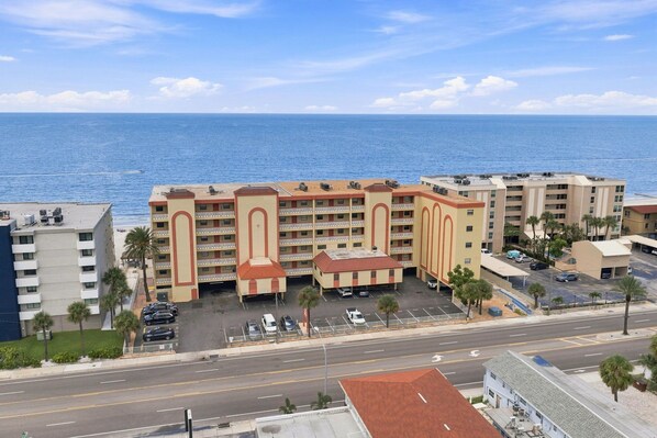 Een hotel met meerdere verdiepingen, een parkeerplaats, uitzicht op het strand en een weg op de voorgrond.