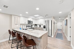 A modern kitchen with a central island, bar stools, stainless steel appliances, and a walk-in pantry.