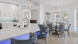 Una cocina moderna con armarios blancos, una isla de mármol y taburetes de bar azules.