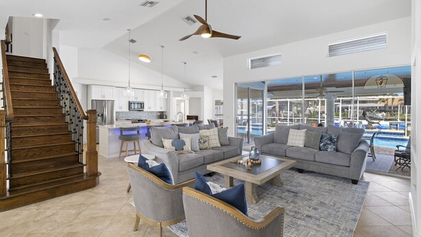 Amplia sala de estar con cocina moderna, una escalera y vista a una piscina.