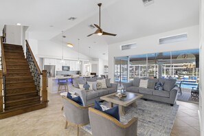 A spacious living area with a modern kitchen, a staircase, and a view of a swimming pool. - Unbeatable Direct Gulf Access Heated Pool Home with a Hot Tub and 6 bedrooms! (Cape Coral)