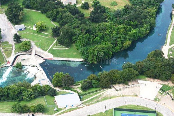 Vista aérea de una zona junto al río, con un puente, cancha de tenis y un pequeño edificio.