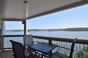 A covered outdoor area with a table and chairs, overlooking a body of water with a distant shoreline.