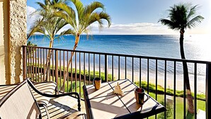 Un balcone con vista sull'oceano, palme, un tavolo con sedie e una tazza.