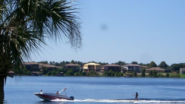 Een meer met een speedboot en een persoon die wakeboardt. Op de achtergrond staan huizen.