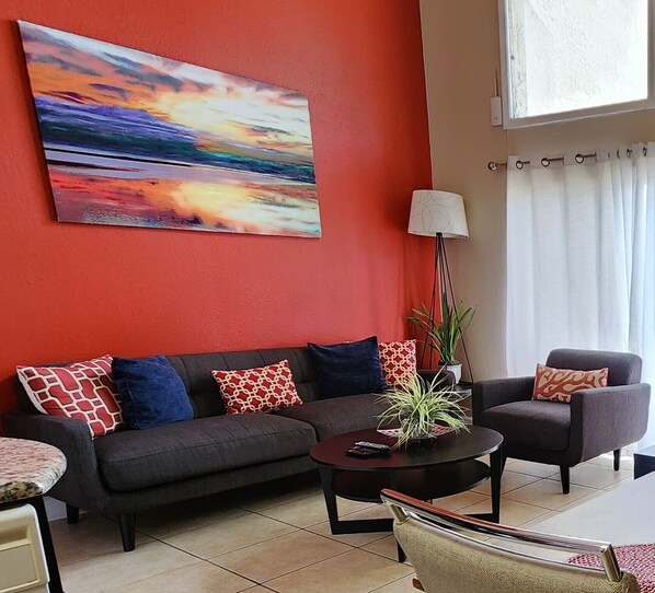 Una sala de estar moderna con una pared de acento roja, un sofá, sillones, una mesa de centro y un cuadro.
