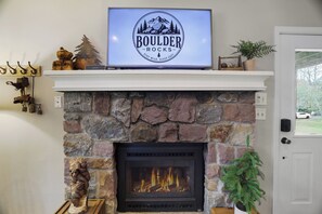 A fireplace with a TV displaying 'BOULDER ROCKS' logo, a stone mantle, and a door with a view of the outside.