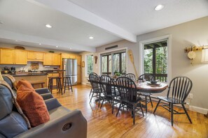 A spacious kitchen with wooden cabinets, a dining area with a round table and chairs, and a large window with a view of trees.